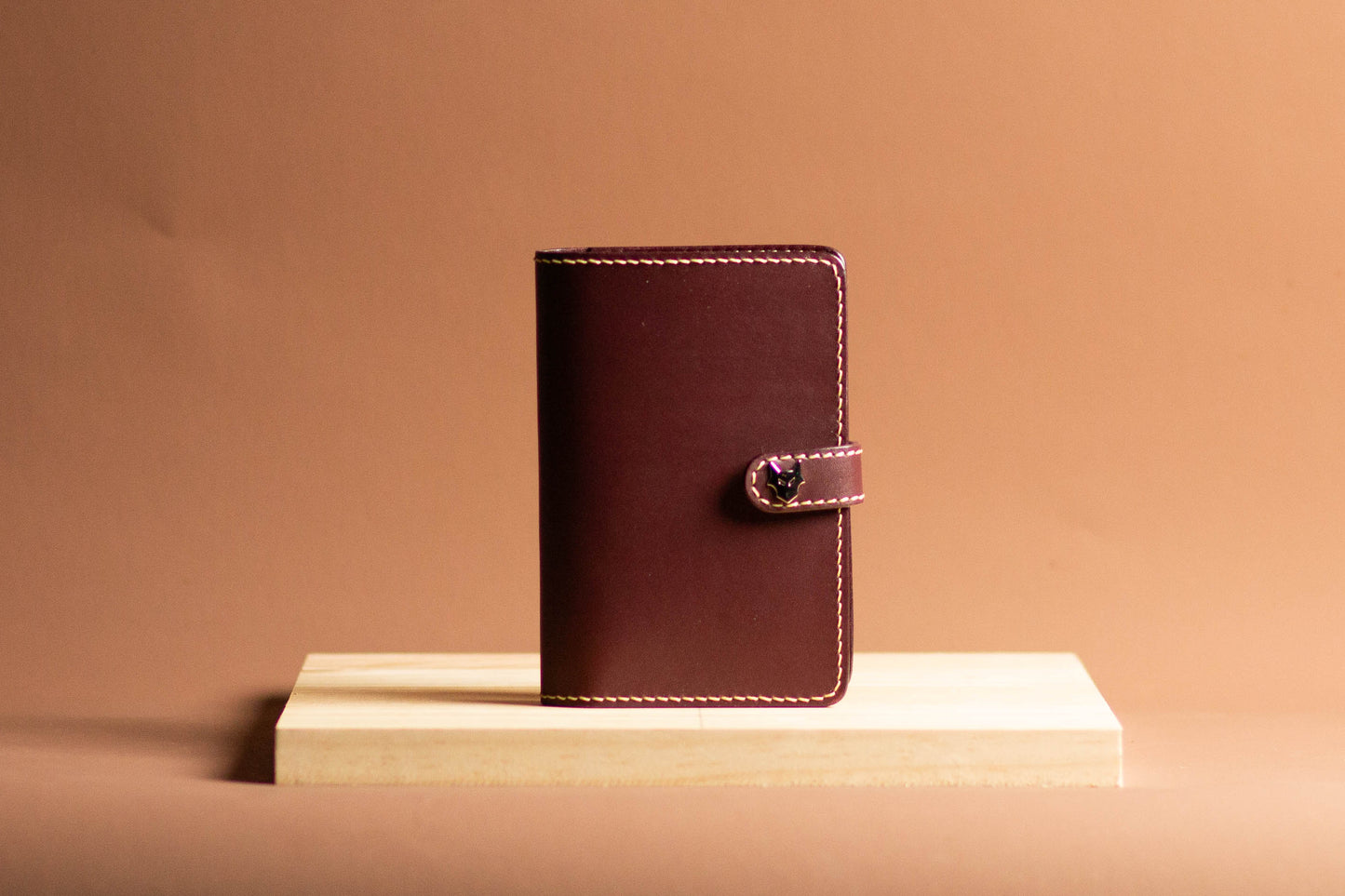 Burgundy leather passport holder wallet on a wooden platform with a beige background