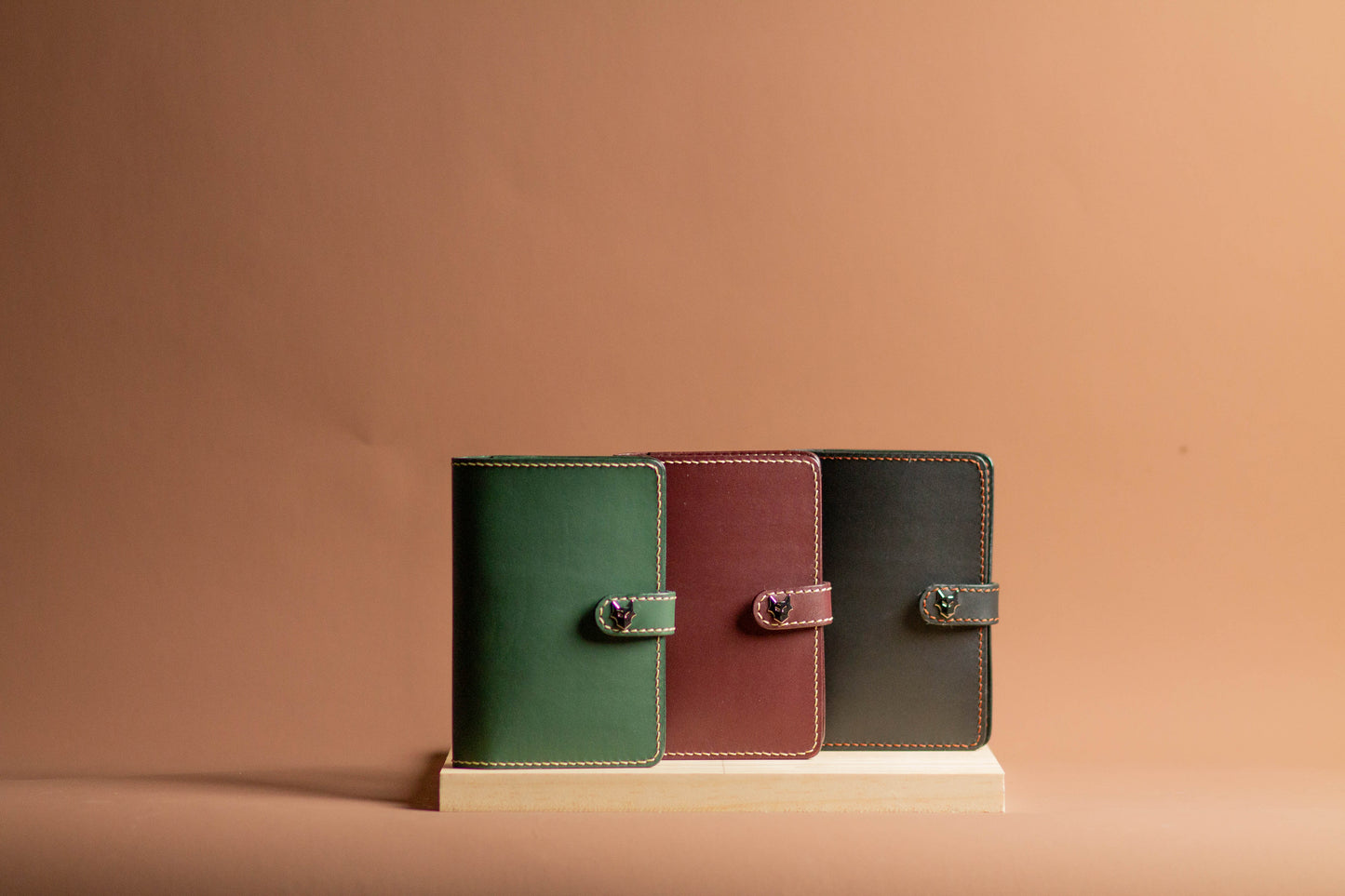 Three leather-bound books in green, red, and black on a beige stand against a beige background