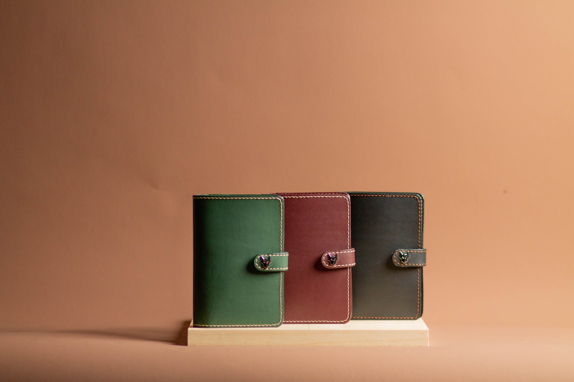 Three leather-bound books in green, red, and black on a beige stand against a beige background
