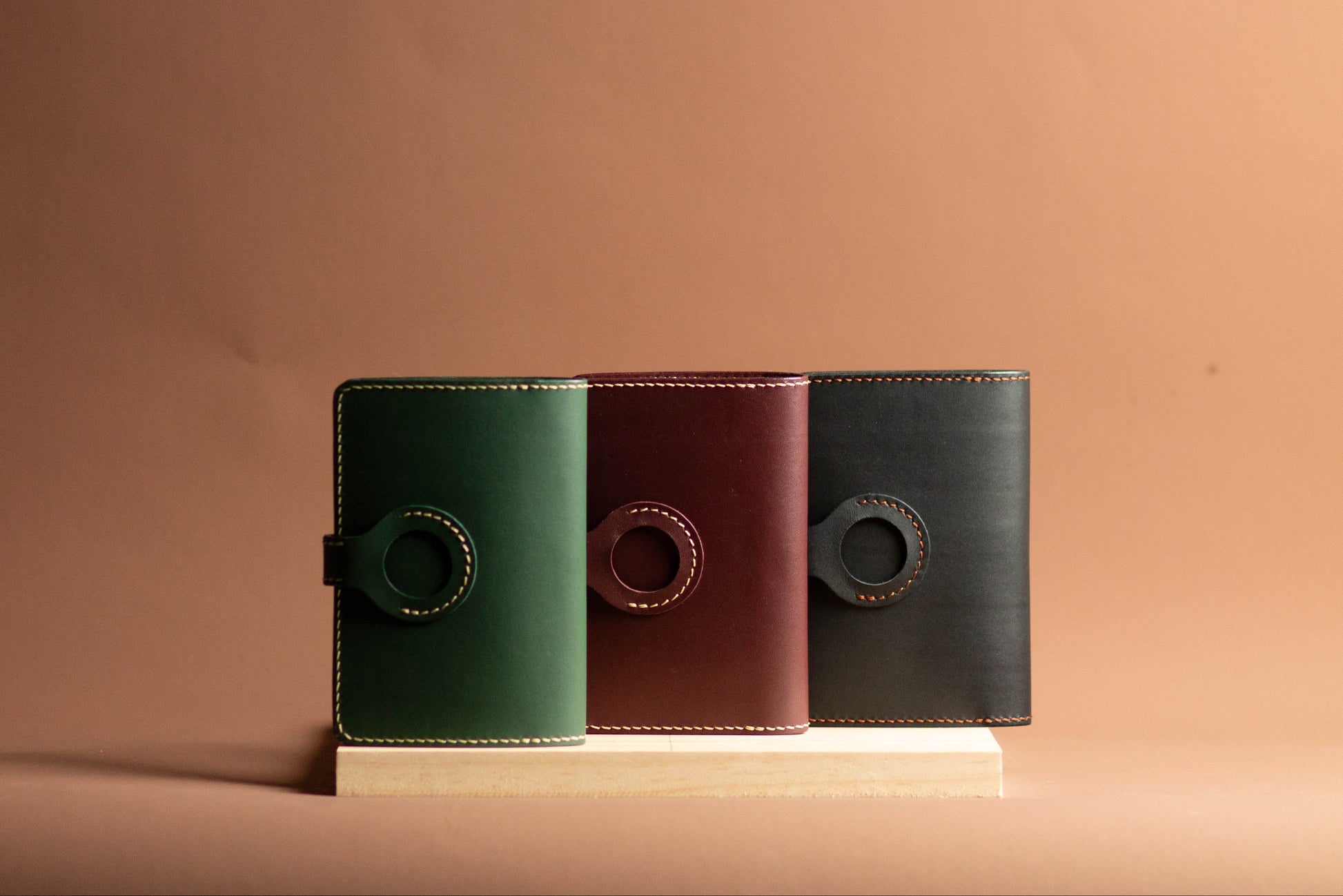 Three leather passport wallets in green, brown, and black on a beige background, showing AirTag compartment 